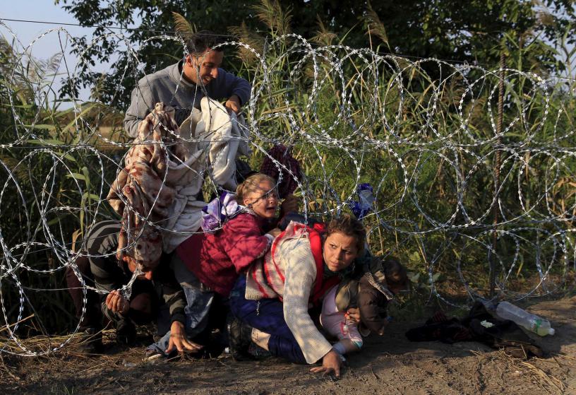 Syrian migrants cross under a fence as they enter Hungary at the border with Serbia, near Roszke, August 27, 2015. Hungary made plans on Wednesday to reinforce its southern border with helicopters, mounted police and dogs, and was also considering using the army as record numbers of migrants, many of them Syrian refugees, passed through coils of razor-wire into Europe. REUTERS/Bernadett Szabo TPX IMAGES OF THE DAY
