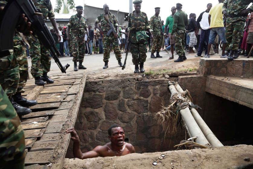 Jean Claude Niyonzima, a suspected member of the ruling party's Imbonerakure youth militia, pleads with soldiers to protect him from a mob of demonstrators after he emerged from hiding in a sewer in the Cibitoke district of Bujumbura, Burundi, Thursday May 7, 2015. Niyonzima fled from his house into a sewer under a hail of stones thrown by a mob protesting against President Pierre Nkurunziza's decision to seek a third term in office. At least one protestor has died in clashes with the widely feared Imbonerakure militias and police, sending scores to the streets seeking revenge. Jean Claude Niyonzima managed to flee from his house under a hail of stones into a covered sewer, where he remained till the army fired shots into the air to disperse the crowd.(AP Photo/Jerome Delay)